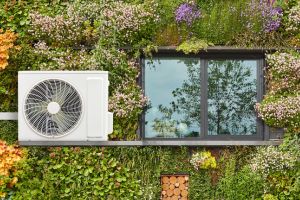 Wärmepumpe an einer begrünten Hausfassade mit Blumen und Fenster.