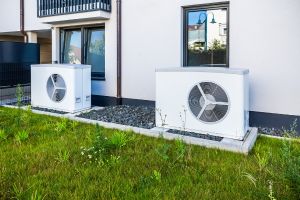 Zwei Wärmepumpen vor einem modernen Mehrfamilienhaus.