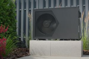 Wärmepumpe im Garten vor einem Metallzaun.