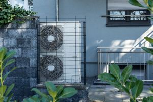 Wärmepumpe hinter Metallzaun an einer Hausfassade.